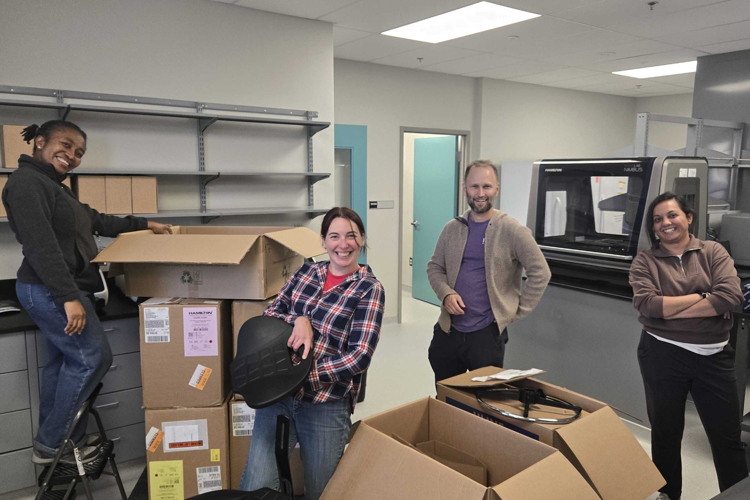 Four lab members smiling while unpacking boxes in the new lab